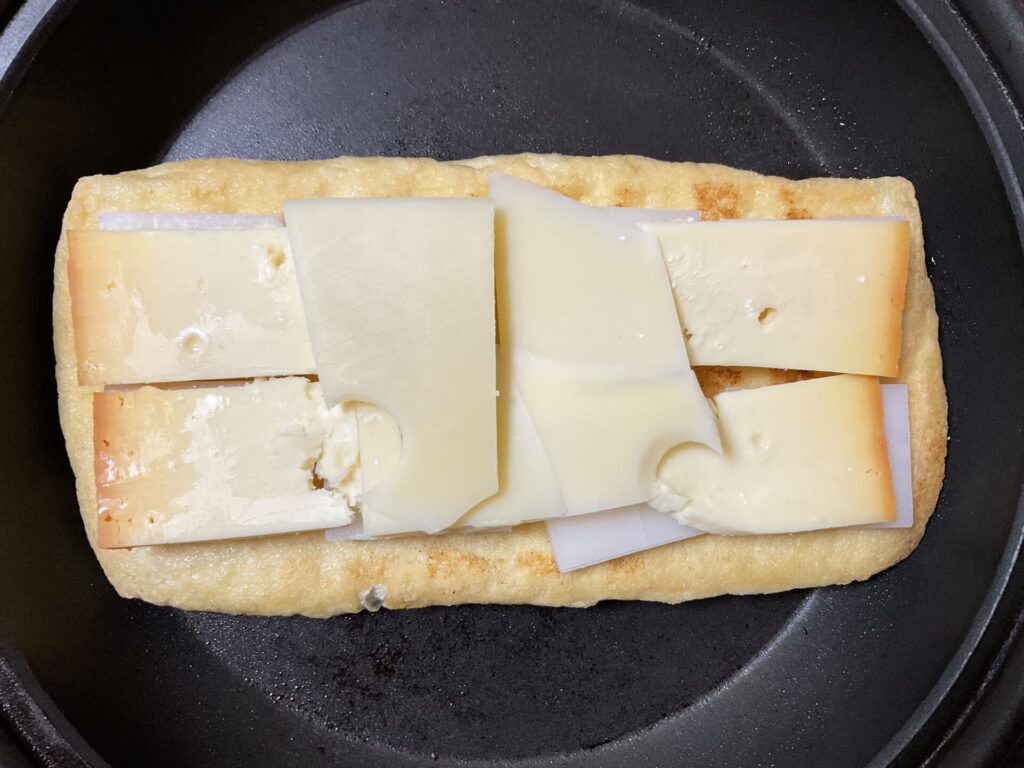 フライパンに入れた油揚げの上に餅とチーズがのせてある
