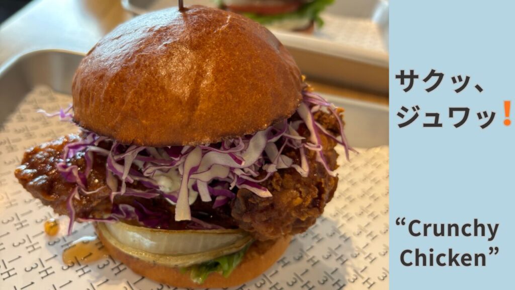 石川県野々市市のハンバーガーショップ「1/3 HAMBURGER FACTORY」チキンバーガーのアップ写真。バンズからはみ出している大きなチキンとソースがたっぷりとかかっている様子。